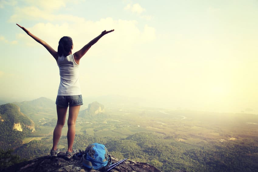 Une femme debout au sommet d'une montagne, les bras tendus, contemplant les avantages et les inconvénients de sa prometteuse carrière à Paris.